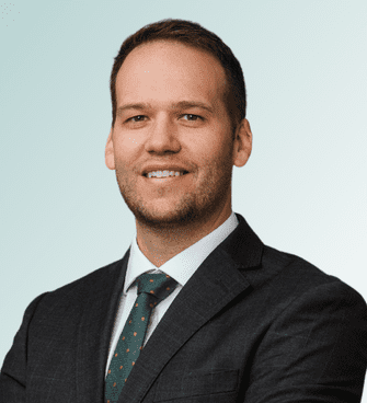 Brian Lancaster A man with short hair, a beard, and a friendly smile is wearing a dark gray suit, white dress shirt, and a dark green tie with a subtle pattern. Dr. Robert FitzGibbons, MD, stands against a light gradient background with his arms crossed.