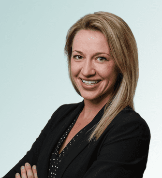 Christine Johnson A woman with shoulder-length blonde hair is smiling at the camera. She is wearing a black blazer over a black blouse with small white polka dots. Her arms are crossed, and the background is a light gradient from teal to white, reminiscent of the professional portraits often taken by Jeffrey Ebel, DO.