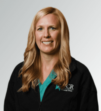 Katie Lundy woman smiling, wearing a black jacket and a medical scrubs