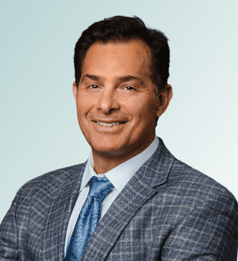 Sean Grey A man with short dark hair, wearing a grey checked suit, a light blue dress shirt, and a blue patterned tie, smiling at the camera against a light gradient background. Dr. Dana Clark, MD, exudes confidence and professionalism.