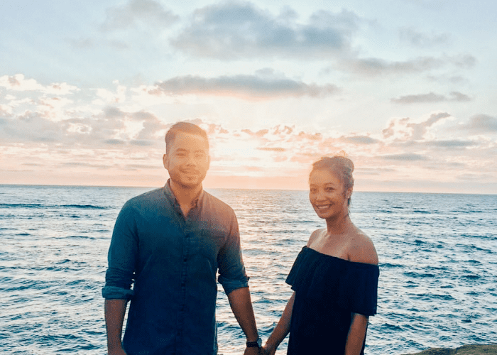 Le 2 A man and woman holding hands in front of a sunset over the ocean