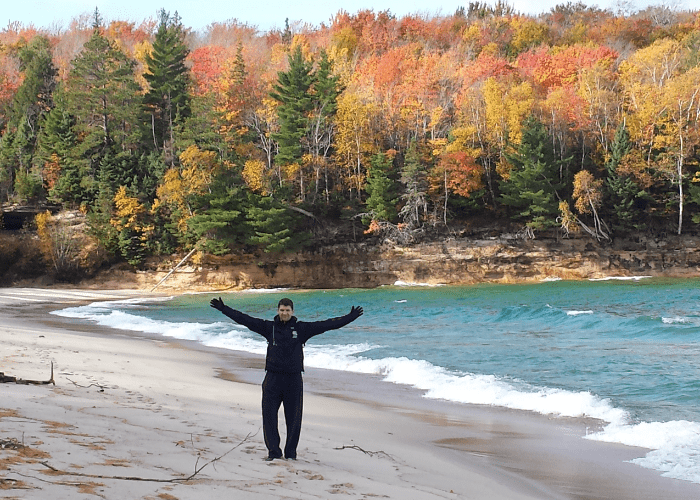 ebel 1 a man standing with his arms open in front of a lake and colorful trees