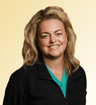 A smiling woman with wavy blond hair stands against a light gradient background. Lindsey Seay, PA-C, is dressed in a black zip-up sweater over a green shirt. A smiling woman with wavy blond hair stands against a light gradient background. Lindsey Seay, PA-C, is dressed in a black zip-up sweater over a green shirt.