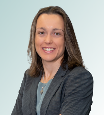 Cara Thorne Cara Thorne, MD, with shoulder-length brown hair, is smiling and looking at the camera. She is wearing a grey blazer over a light blue blouse, with a necklace visible. The background is a gradient of light blue to white.