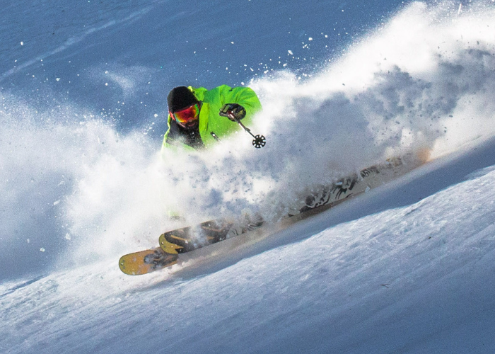 Dr. Suwak Skiing A skier dressed in a bright neon green jacket, black pants, and a black helmet is captured mid-action while skiing down a snowy slope. Snow sprays dramatically around them, highlighting the skier's dynamic movement through the fresh powder.