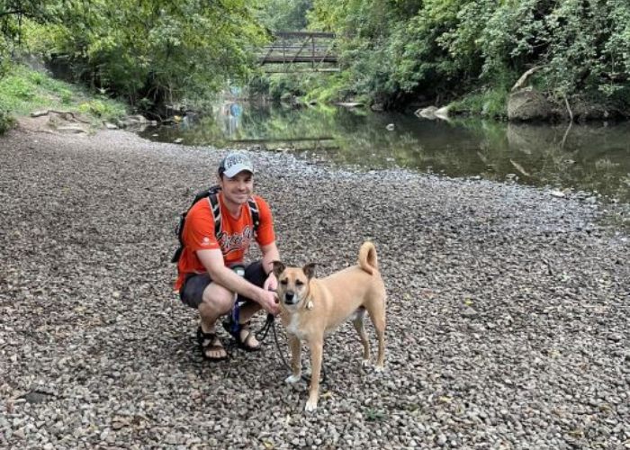 Dr. Johnson & Dog Dr. Johnson sits on a gravel trail in front of a river with his dog.