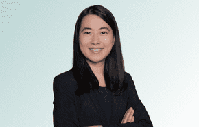 provider A woman with long dark hair, wearing a black blazer and black top, smiles with her arms crossed against a light blue gradient background.