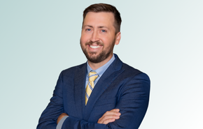 provider A man in a blue suit with a yellow striped tie stands smiling with arms crossed against a light gradient background.