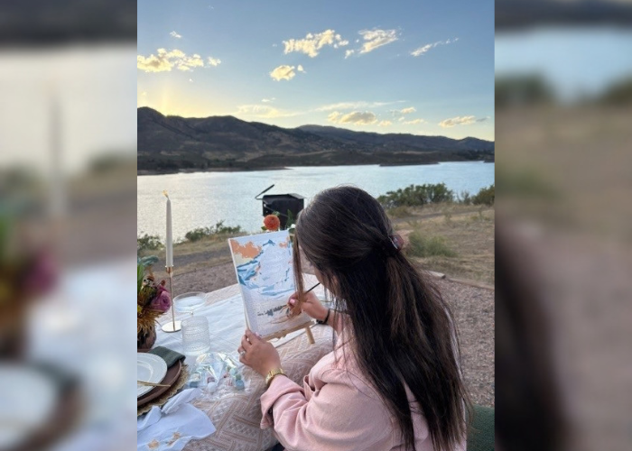 Dr. Machado sitting at a picnic table facing Horsetooth Lake water painting