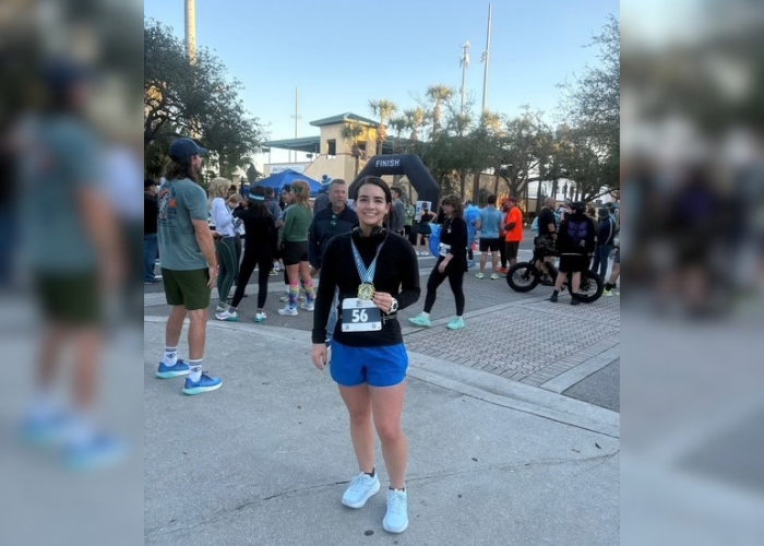 Dr. Machado standing in a black long sleeve and blue shorts holding a medal