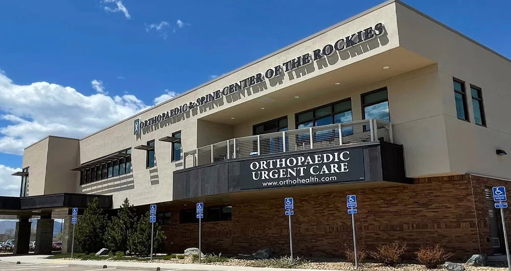 A modern two-story medical building with large windows and a sign reading "Orthopaedic & Spine Center at Chulahoma," featuring a covered entrance and an empty parking lot with marked handicap spaces.