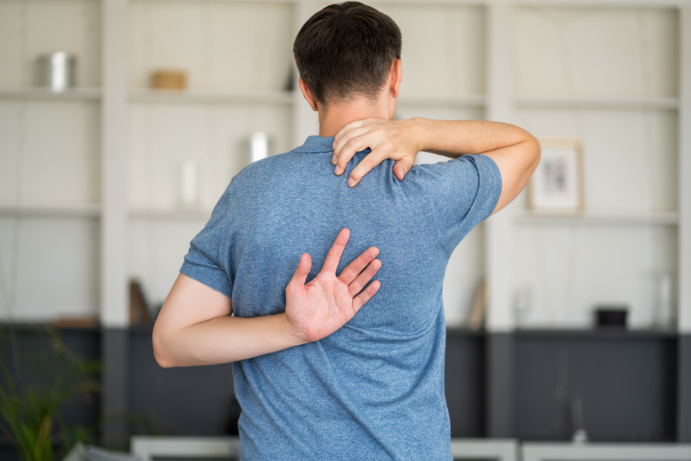 A person in a blue shirt is facing away, stretching by reaching one hand over their shoulder and the other behind their back—an exercise often used in ACL tear recovery.