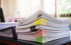 featured-papers A large stack of documents with colored sticky tabs sits on a desk, with sunlight streaming through windows in the background.